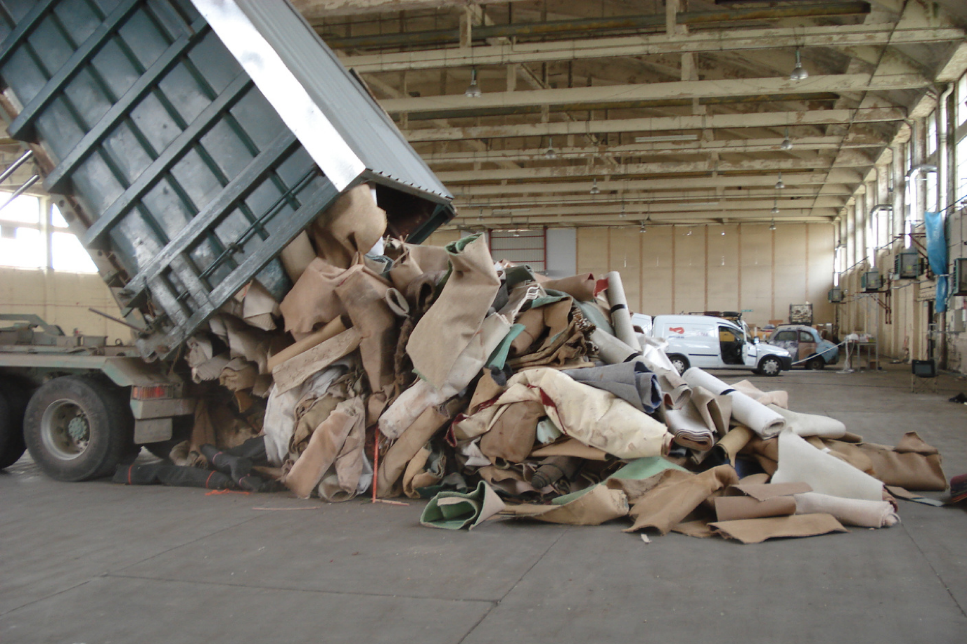 Image of a lorry emptying used carpets into the centre of a warehouse floor. Vans and doors of th distribution centre can be seen in th background.