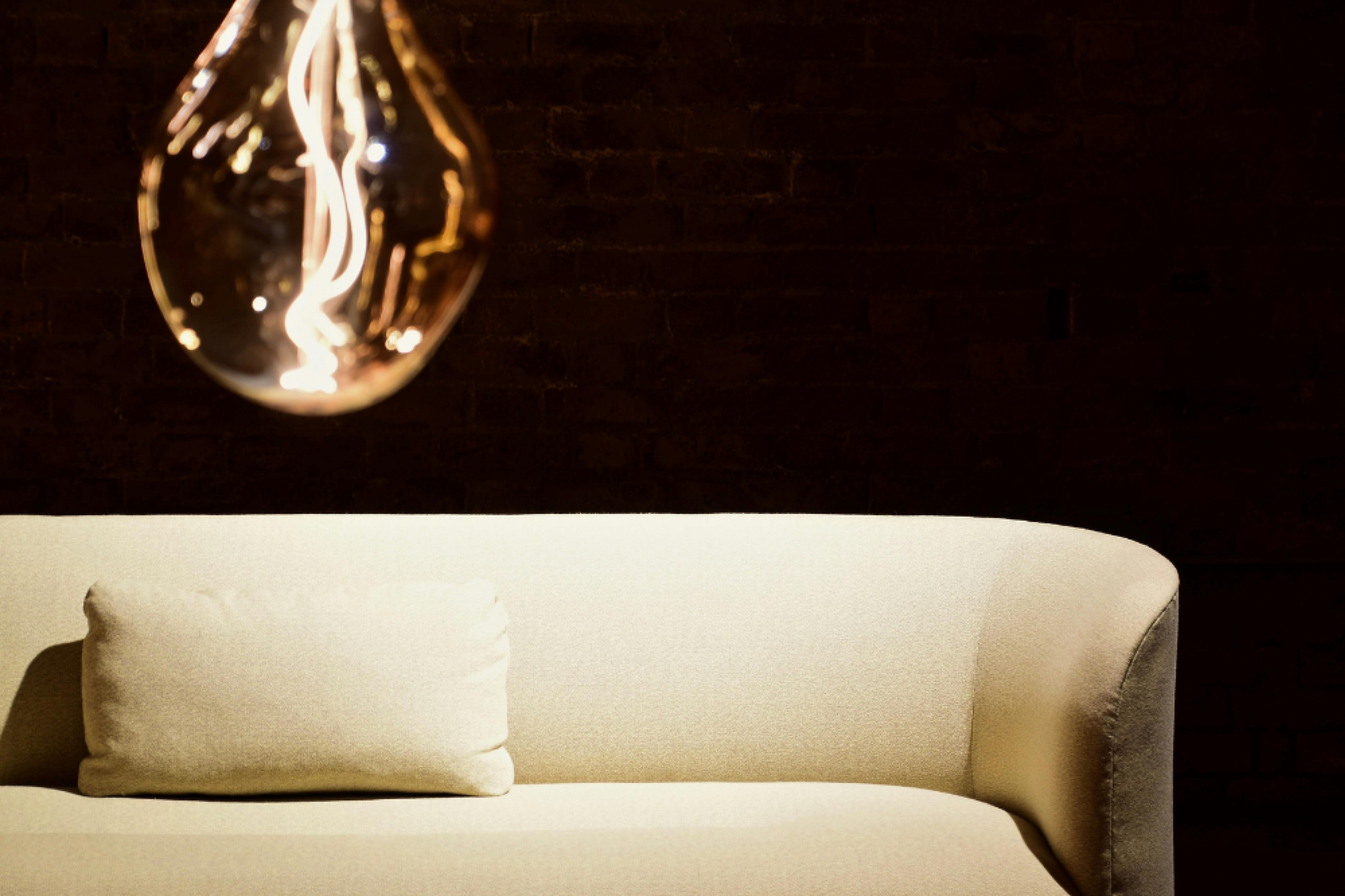 A cream sofa and solitary cushion feature against a black background. An image of a lightbulb features left centre, dominating the image.
