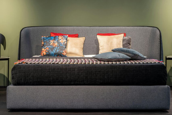 a grey upholstered bed with colourful cushions
