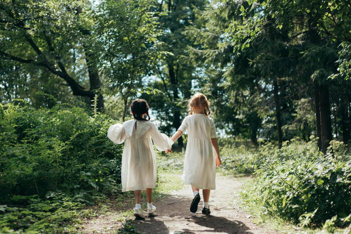 Two children wearing white dresses in a woodland setting