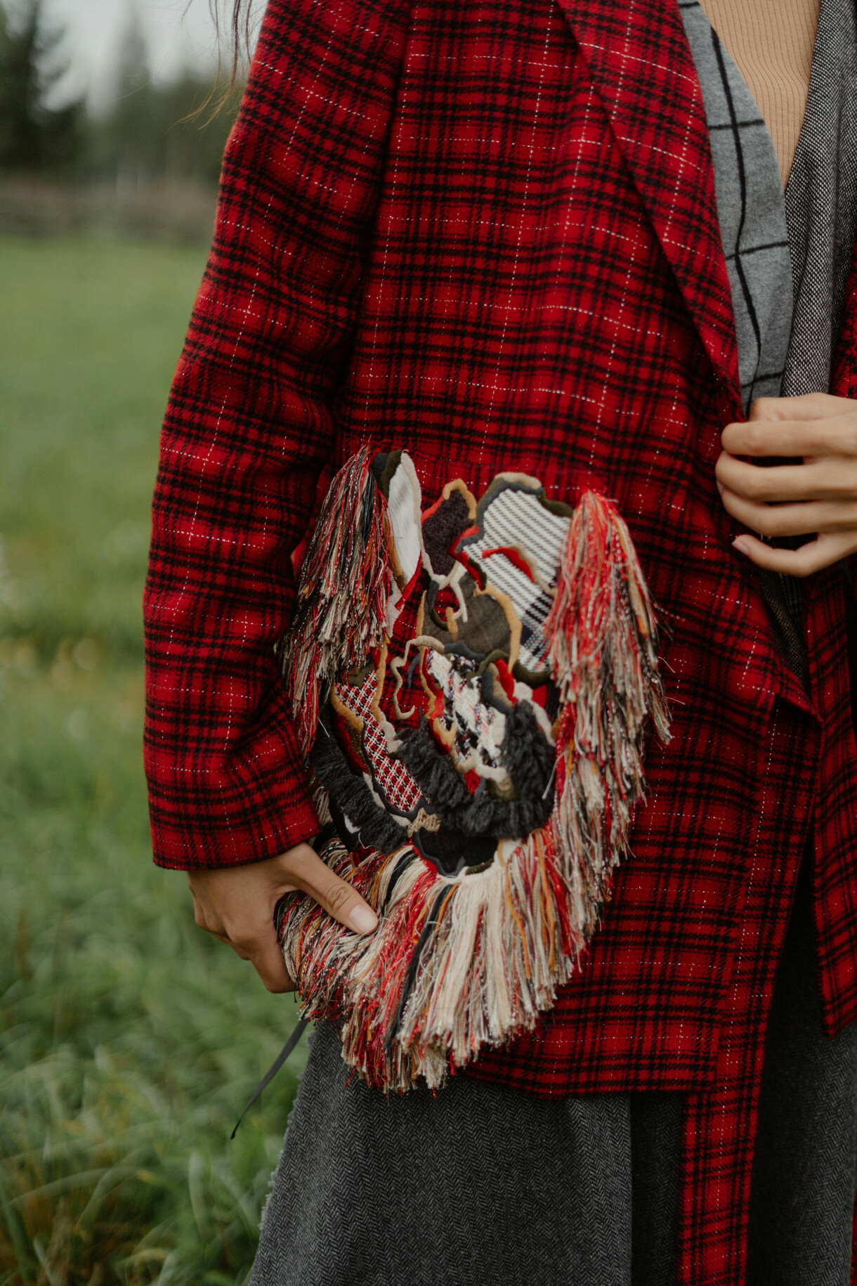 A close up of a fashion model in a red check jacket holding a tapestry clutch bag